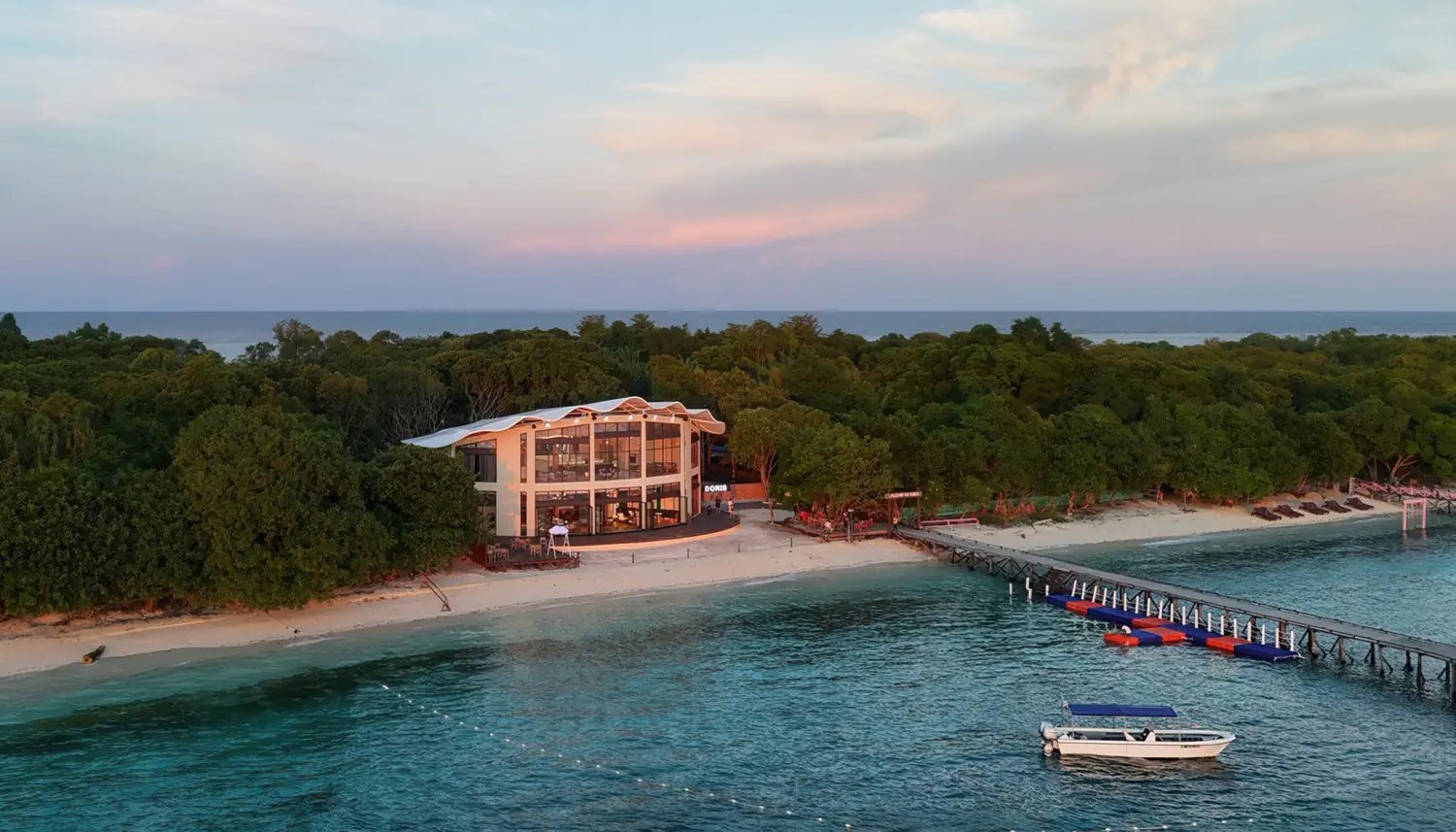 Aerial view at dusk of a glass-fronted building on the beach, a jetty and a boat, Doris Mataking Resort, Mataking Island